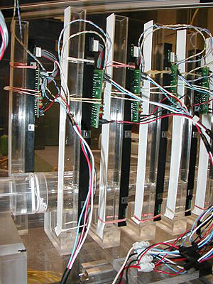 Figure 6. Photo. CIS sensors attached to standpipes. This photo shows a closeup of the instrumented standpipe configuration. Each standpipe is equipped with sensors and circuit cards, with wires that communicate the measurements to a nearby computer. The photo further shows how water may enter the standpipe from the bottom of the inflow or outflow pipe where it can rise in the standpipe so its level may be recorded with the CIS instrument. 
