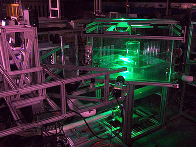 Figure 9. Photo. Access hole setup with P I V light sheet in outflow pipe. This photo is an overall view of the experiment setup with the laser in operation. The room is dark, and the Plexiglas box surrounding the access hole is approximately half full with clear water, while the water in the access hole is fluorescent. The light sheet in the outflow pipe is the brightest object in the image.