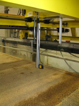 Figure 54. Photo. Automated point laser distance sensor (side view). This photo shows the instrument attached to the instrument carriage and extending down toward the sand bed in the flume in position to collect distance data when the experiment is underway.