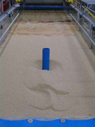 Figure 56. Photo. Bed bathymetry after a pier scour test. This photo shows a scoured bed, which has a hole at and around the pier and a deposition of material downstream of the pier model.