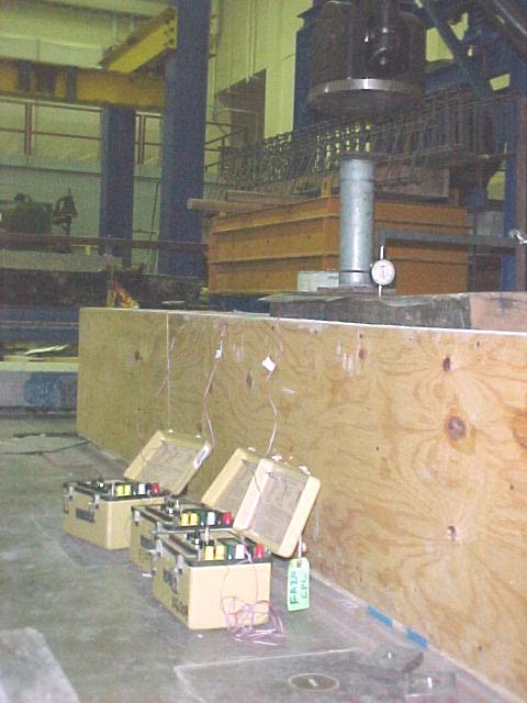 This photo shows an experimental setup where the fiber reinforced polymer (FRP) dowels were initially tested in timber beams before testing them in concrete pavement slabs. Tests were conducted on the timber beams using dowel bars mounted with longitudinal and transverse gauges. The load was applied through a loading frame, and the strain and deflections were recorded through a strain indicator and a dial gauge.