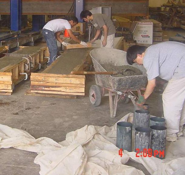 This photo shows graduate students casting concrete cylinders and beams using plastic cylinders and wood formwork in a laboratory. 