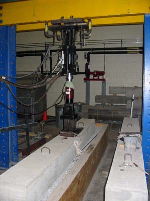 This photo shows the experimental setup with the slabs being positioned on top of an aggregate-filled rectangular wooden bin representing the subgrade. Load is being applied to one of the slabs near the joint with a 244.652 kN (55 kip) hydraulic actuator system suspended from a loading frame.