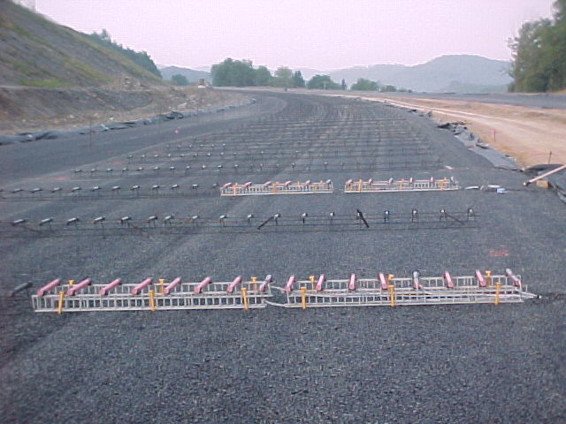 FRP dowel bar installation is shown in this photo at location 1 of corridor H project on Route 250, Elkins, WV. Two alternate rows of 16 fiber reinforced polymer (FRP) dowels each were placed on plastic baskets and anchored onto subgrade on the right side of the lane in the photo. The remainder of the dowel baskets in the right and left lanes are made of steel.