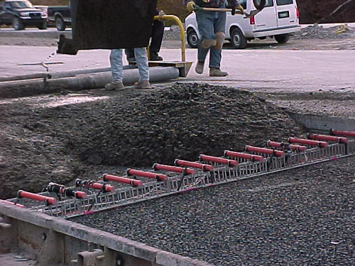 This photo shows pavement construction as fiber reinforced polymer dowel bars supported on plastic baskets placed on the subgrade are being covered with concrete.