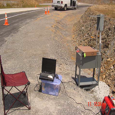 This photo shows the data acquisition system connected to strain gauges on fiber reinforced polymer dowel bars and embeddable concrete gauges in the pavement through a junction box on the roadside consisting of all wires from the pavement. Laptop computer, data acquisition unit, and a portable generator are also seen.