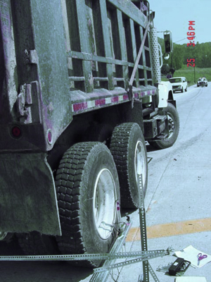 This photo shows the rear wheels of a loaded West Virginia Department of Transportation (WVDOT) truck which is positioned near the pavement joint for load testing. Linear variable differential transformers used for measuring deflection are supported on a metal frame.