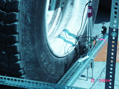 This photo shows a close up view of figure 77 where rear wheels of the loaded West Virginia Department of Transportation truck are positioned near the pavement joint for load testing. Also visible are linear variable differential transformers (LVDT) used for measuring deflection across a joint, which are supported on a metal frame.