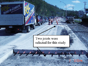 This photo shows the fiber reinforced polymer (FRP) and steel dowel bar locations in a pavement with concrete removed for rehabilitation purposes and dowels inserted into the visible pavement cross sectional area of the right lane. Two of the joints selected for rehabilitation of an existing pavement near junction of Route 119 and Route 857, University Avenue, Morgantown, WV, are shown, and vehicular traffic is seen on the adjacent left lane. 