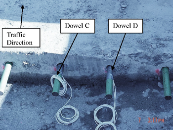 This photo shows steel dowel bars that are positioned in the pavement slab where a portion of concrete is sliced and removed for rehabilitation. Two wires attached to strain gauges of dowel bars, designated as dowel C and dowel D, as well as the traffic direction are shown.