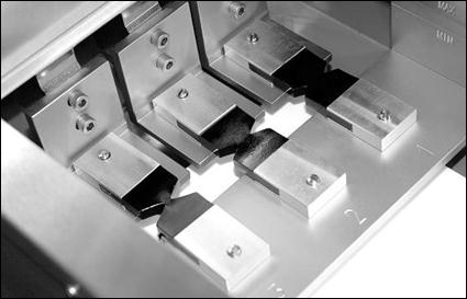 This photo shows three double-edged notched tension (DENT) test specimens with different ligament lengths loaded in the ductilometer instrument before tensile loading begins.