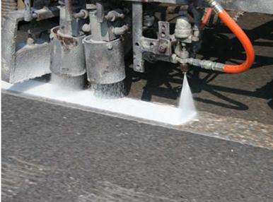 This photo shows a close-up view of pavement marking material being sprayed on the roadway.