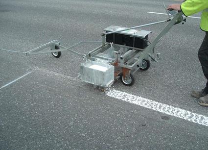 This photo shows a worker applying structured methyl methacrylate (MMA) to a roadway.