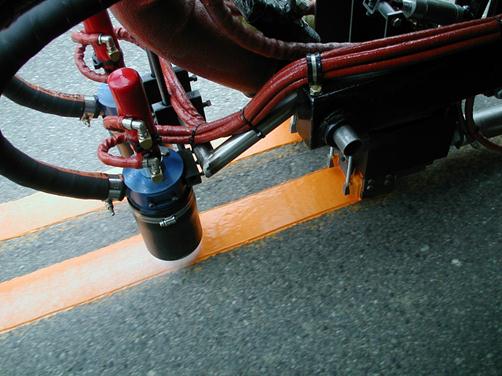 This photo shows glass beads being applied with a bead gun on thermoplastic on a roadway.