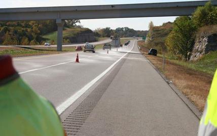 This photo shows glass beads being applied on a highway. A dusting of beads can be seen extending beyond the edge line and across the road surface.