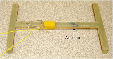 This photo shows a second prototype antenna adapted to the H-shaped gauge. It is yellow and in the shape of a horizontally stretched H. In the center, there is a yellow band that has two yellow strings extending from it.