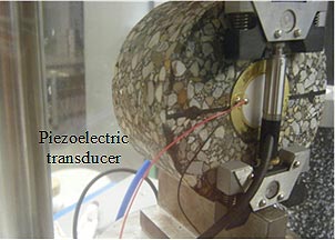 This photo shows a close-up view of the asphalt specimen in the apparatus and the piezoelectric transducer, which is a small cylindrical object that sits next to the specimen during the test.