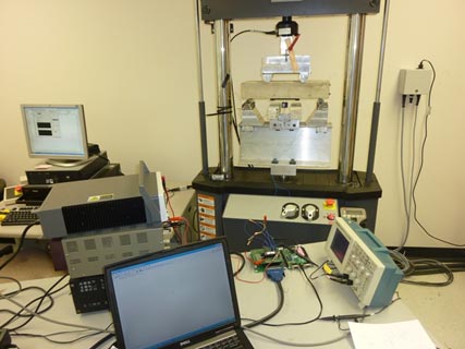 This photo shows a concrete beam placed in a test apparatus and a computer that records the results of the test.