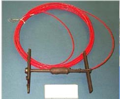 This photo shows an example of an asphalt strain gauge. It is a red wire coiled up with an end attached to a bronze H-shaped piece of metal.
