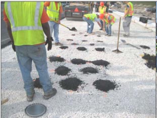 This photo shows construction workers placing screened asphalt on top of gauges and carefully compacting them.