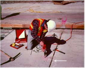 This photo shows a construction worker making grooves in the cement-treated base for instrument leads.