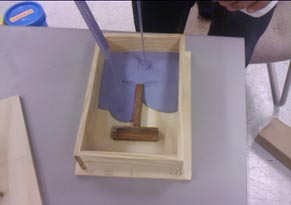 This photo shows violet silicon being poured into a box and over a wooden "H."