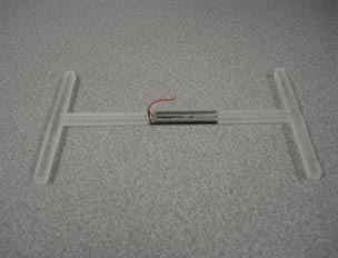 This photo shows the piezoelectric transducer embedded in epoxy. The epoxy cast is H-shaped stretched horizontally, and the piezoelectric transducer is a small, black, rectangular piece that sits in the middle of the "H" shape.