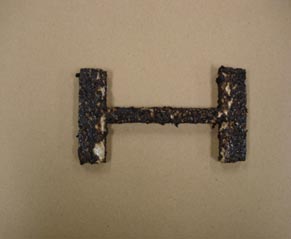This photograph shows an H-shaped specimen in a slab compactor. The specimen is surrounded by black asphalt concrete.