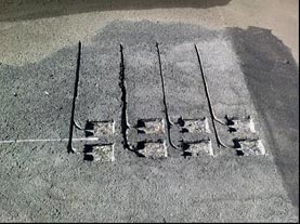 This photo shows cut-out shapes in the cement for the sensors and wires. There are two rows of four, with a line drawn indicating the tire track running down the middle of the rows.