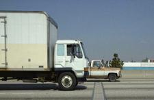 This photo shows a weigh-in-motion (WIM) sensor. Two vehicles are shown traveling on a highway from left to right. In the forefront is single-unit truck. Another truck that is traveling in an inner lane and slightly ahead of the single-unit truck is also seen. 