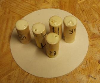 This photo shows five pipes that contain a tag that were then filled with epoxy and cured on a circular piece of paper. The pipes are placed vertically with the air bubbles at the top of the pipes.