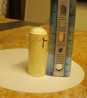 This photo shows a single pipe placed on the circular piece of paper in the vertical position. At the top of the pipe is a dome formed from the extrusion of epoxy. A ruler next to the pipe shows the extrusion is approximately 0.25 inches high.