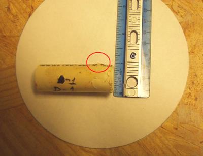 This photo shows a single pipe placed on the circular piece of paper in the horizontal direction. At the top right side of the pipe, a bulge is circled. A ruler next to the pipe indicates size. The bulge is approximately 0.125 inches.