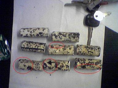 This photo shows eight tags. The tags are placed in three rows. The top row contains two tags, and the middle and bottom rows contain three tags. At the top right corner of the photo, a set of keys is used to show size comparison. The tags are about the same size as the car key. All three tags in the bottom row have red ovals indicating bulges. The first two have bulges at the top of the tag, and the right-most tag has a bulge all the way down the bottom side. The middle tag in the middle row has a bulge in the top left part of the tag.