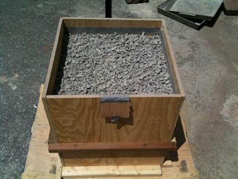 This photo shows a wooden box containing coarse aggregate from an angled view, showing both the box from the side and top. There are no visible tags because they are all covered with the coarse aggregate.