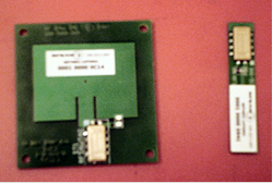 This photo shows two radio frequency identification tags. The tag on the left (single patch) consists of a large rectangular plate with four holes in each of the corners. Within this large rectangle is a smaller rectangle placed near the top of the larger rectangle that extends about two-thirds of the length of the larger rectangle. At the bottom of the larger rectangle is the receiving antenna that consists of a metal rectangle placed on top of a chip. It appears that two black rods are extending from this. The tag on the right (monopole) is the same height as the single patch tag but is about oneÂ­ fifth of the width. At the top of the tag is the receiving antenna, which consists of a metal rectangle placed on top of a chip. It appears that two black rods are extending from this.