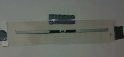 This photo shows the dipole antenna that is made of both silver and carbon conductive paint. The antenna is in the horizontal position. The radio frequency identification (RFID) chip and antenna are located in the center. The 0.8 inches of the antenna closest to the RFID chip is painted with carbon, and the rest of the dipole length is painted with silver paint. This was also done on a flexible plastic substrate.