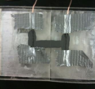 This photo shows the two polymethyl methacrylate (PMMA) sheets that are attached to the bottom of the beam. The sheets just touch each other. A wire extends from each of the sheets toward the top. The wire is covered in Aquadag® E™ and is connected with another line of Aquadag® E™. There are pieces of duct tape at the top and bottom of each wire on each sheet.