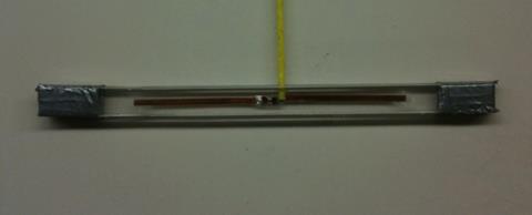 This photo shows the symmetric dipole antenna with sides of 3.2 inches each. The antenna is in the horizontal position. The radio frequency identification chip and antenna are located in the center. The dipole tag is sandwiched between two thin polycarbonate pieces. A wooden toothpick is sandwiched between the polycarbonate pieces on top of the overlap.