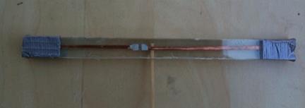 This photo shows the dipole antenna with sides of 3.2 inches and 2 inches. The antenna is in the horizontal position. The RFID chip and antenna are located to the left of the 2-inch side, followed by the 3.2-inch side. The dipole tag is sandwiched between two thin polycarbonate pieces. A wooden toothpick is sandwiched between the polycarbonate pieces on top of the overlap.