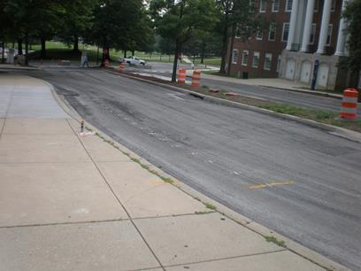 This photo shows the placement of the encapsulated tags in a roadway. It appears that the roadway has been milled. The tags are placed longitudinally 2 ft apart along the roadway. The locations of the tags are indicated by spray paint, and the protective polycarbonate surrounding the tags can be seen.