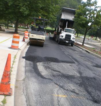 This photo shows the paving of the roadway where the sensors were placed. A dump truck with asphalt is unloading into the asphalt paving machine on the right-hand side of the photo while the steel wheel roller is compacting the asphalt shown on the left-hand side of the photo.