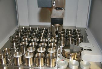 This photo shows the interior of the x-ray fluorescence spectrometer,  the 52 sample stations where the steel cup holders reside, the crane lifting  them into the x-ray chamber, and the x-ray chamber itself.