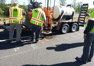 Figure 25. Photo. Pavement coring for sensor installation. This photo shows workers on a roadway marking the locations of the sensors and coring the pavement.