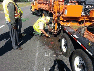 Figure 26. Photo. Smoothing of holes for sensor installation. This photo shows workers on a roadway smoothing the bottom of the holes created for sensor installation with an air hammer.