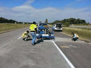 Figure 30. Photo. Sensor verification with FWD. This photo shows workers verifying the performance of each sensor using a falling weight deflectometer (FWD).