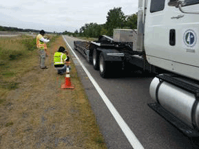 Figure 35. Photo. Verifying the embedded sensor alignment. This photo shows workers on the side of a roadway verifying the feasibility of aligning the tires of the moving deflection devices with the sensors using the MnROAD instrumented truck.