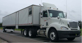 Figure 1. Photo. ARA RWD. This photo shows the Applied Research Associates, Inc. (ARA) Rolling Wheel Deflectometer (RWD). The photo depicts the RWD, which is comprised of a 53-ft (16.15-m)-long trailer used to collect data as it travels along an asphalt pavement. There is an apparatus extending from the rear of the trailer to a distance roughly three-quarters to the front of the trailer that contains the four lasers used by the RWD, which are 8 ft (2.44 m) apart.