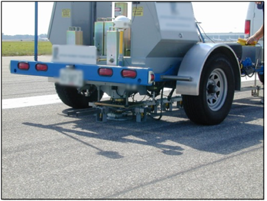 This photo shows a Dynatest® FWD device in use. Weights and sensors are shown on the pavement under the device trailer.