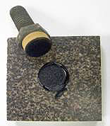 Figure 3. Photo. Pull-off test specimen on diabase stone after testing. The loading fixture and stone substrate are shown. The test sample was tested in the dry condition and failed cohesively within the mastic film as evident by the fact that mastic is observed on the ceramic surface of the loading fixture and on the diabase substrate.